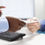Closeup of elderly man receiving medical advice from doctor holding onto piece of paper. African american doctor providing written recovery process instructions to caucasian patient in clinic office.